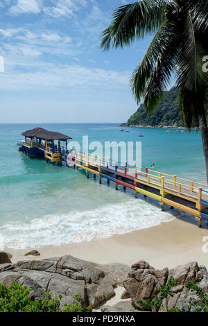 Calcestruzzo colorato e pontile in legno sporgente su una spiaggia di sabbia bianca di un blu limpido mare calmo, rocce e alberi su entrambi i lati il cielo è blu con whi Foto Stock