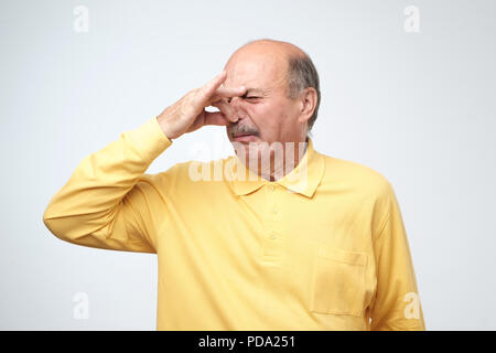 Coppia uomo caucasico in giallo tshirtwith disgusto sul suo volto pizzichi di naso. Qualcosa puzza, molto cattivo odore. Emozione negativa espressione facciale Foto Stock