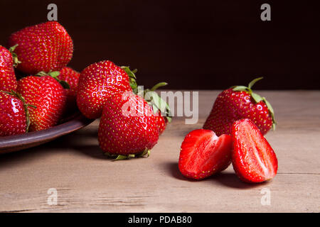 Dolce con fragole a fette, semi e frutti interi su sfondo vintage. Piastra di argilla con fresche e mature di bacche rosse di fragole su sfondo di legno. Foto Stock