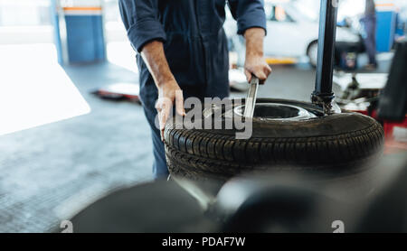 Le mani del meccanico rimozione di pneumatici vettura dal disco sulla macchina. Uomo al lavoro sulla macchina per la rimozione di gomma dal cerchio in negozio di riparazioni auto. Foto Stock