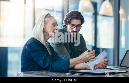 Donna matura e giovane uomo a discutere di lavoro in ufficio. Imprenditrice titolari di una carta in mano mentre prendendo al suo collega di sesso maschile. Foto Stock