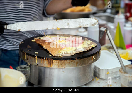 Preparare crêpe, galette con prosciutto, formaggio e uova sulla piastra nera. Lo Chef le mani, estate città parte. Concetto nazionale, cibo molto gustoso il fast food, Summer Party Foto Stock