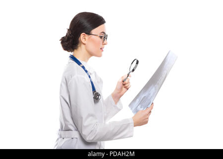 Giovane donna medico con stetoscopio cerchi a raggi x effettuare diagnosi in divisa bianca su sfondo bianco Foto Stock