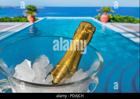 Vacanza di Lusso bottiglia di champagne su ghiaccio, di refrigerazione in vetro cristallo dello scambiatore di calore del vino sulla terrazza con la vacanza di lusso piscina infinity e la costa del mare vista dietro Foto Stock