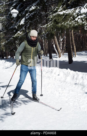 UFA, Russia 29marzo 2018 - giovane uomo casual in jeans e cappotto invernale Sci di fondo attraverso una pista forestale in nevicata utilizzando sport di inverno di imp Foto Stock