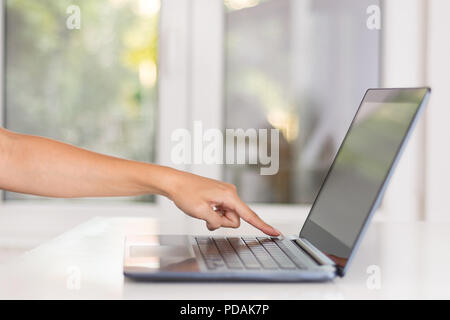 Ragazza della mano e del dito premendo il pulsante sul notebook nero in ufficio. Lavoro moderno e concetto di lavoro. Close up, il fuoco selettivo Foto Stock