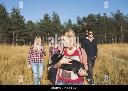 Piccolo gruppo di giovani godendo all'aperto con la bella black bulldog francese. Giornata di sole. Natura della montagna. Foto Stock