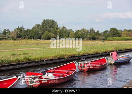 Giethoorn, Paesi Bassi - 1 Agosto 2018: un ragazzo adolescente vele il canal e raccoglie il dipinto di rosso electric noleggio barche alla fine di un'estate dopo Foto Stock