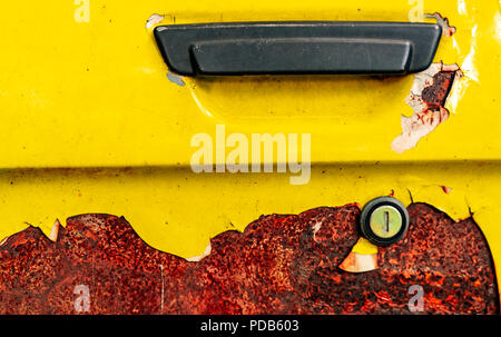 Chiudere la vecchia auto porta con arrugginito. Abbandonato rusty giallo auto con impugnatura nera. Colorazione di auto è la pelatura. Vecchie e arrugginite porta di automobile backgr texture Foto Stock