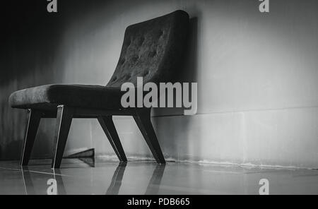Nero sedia classica con design unico nella vuota stanza di riposo vicino al muro di cemento sulla oscura e drammatica dello sfondo. Premuto, triste e solitaria concetto. Uno e Foto Stock