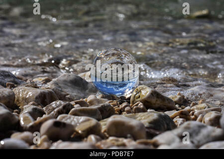 Palla di vetro seduto alla spiaggia rocciosa whit mare onda riflessa in esso/ immagine concettuale delle vacanze estive Foto Stock