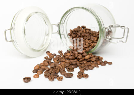 Top in vetro nella conservazione di alimenti jar giacente sul lato isolato su sfondo bianco con chicchi di caffè tostati fuoriuscita Foto Stock