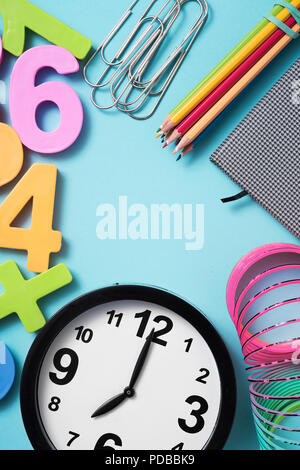 Un orologio a sette, alcuni Pencil Matita colorata di colori differenti in un notepad, alcuni clip di carta e alcuni tridimensionale di numeri di differenti colori su un blu Foto Stock