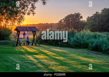 Germania, Guthaus Stolpe Station Wagon.Gutspark e tramonto sul fiume Peene con la donna seduta e pesca matura. Gutsh Foto Stock