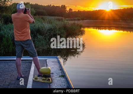 Fotografo maschio tenendo fotografia del tramonto sul fiume Peene in Peenetal natura park, Gutshaus Stolpe station wagon, Germania Foto Stock