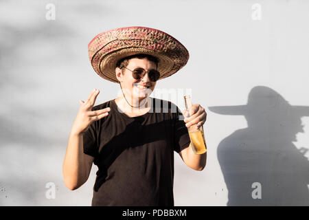 Giovane maschio persona in sombrero vaso di contenimento della bevanda. Indipendenza del Messico festosa concetto di uomo che indossa national Mexican Hat partying Foto Stock