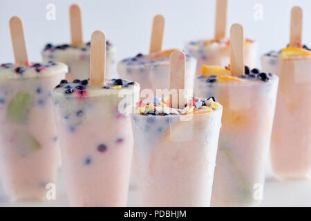 Vista ravvicinata di dolce popsicles fatti in casa con frutti e bacche in contenitori su grigio Foto Stock