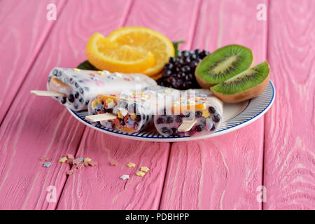Vista ravvicinata di popsicles fatti in casa con frutta fresca e bacche sulla piastra rosa sul tavolo di legno Foto Stock