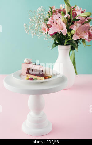 Pezzo di torta con marshmallow e caramelle sulla torta di stand e bouquet di fiori in vaso Foto Stock