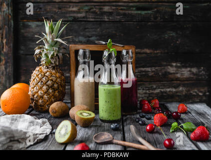 Organici frullati di frutta in bottiglie di vetro su sfondo di legno con frutti assortiti Foto Stock