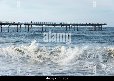 Surfer in mare accanto al molo cambs sulla costa del North Yorkshire, Inghilterra. Foto Stock