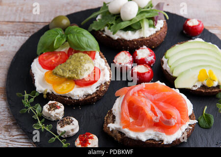 Varietà di crostino con salmone, avocado, mozzarella, pomodoro, pesto,olive, crema di formaggio. Mix di diversi spuntini e stuzzichini Foto Stock