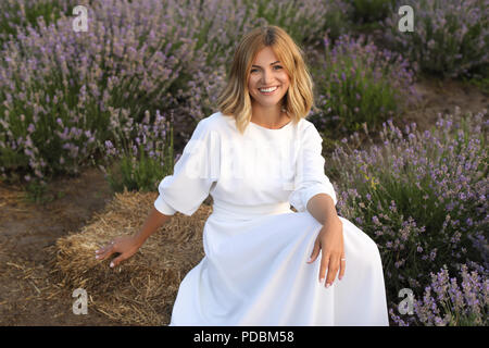 Donna attraente in abito bianco seduta sulla balla di fieno in viola campo di lavanda Foto Stock