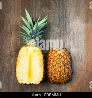 Ananas frutta tagliata due metà superiore sullo sfondo di legno lo spazio negativo. Composizione quadrata. Succosa coltivati biologicamente mature e dolce Foto Stock