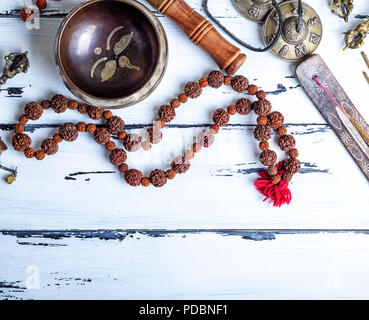 Il rame Singing Bowl, grani di preghiera, preghiera tamburo e altre religiose tibetane oggetti per la meditazione e la medicina alternativa su un bianco backgroun in legno Foto Stock