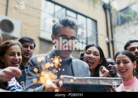 Amici celebrando con uomo con torta di compleanno Foto Stock