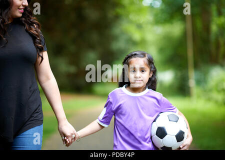 Ritratto ragazza con pallone da calcio tenendo le mani con la madre Foto Stock