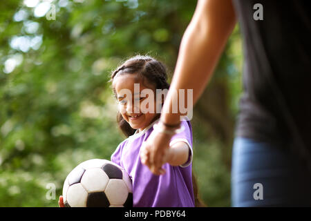 Ragazza sorridente con pallone da calcio tenendo le mani con la madre Foto Stock