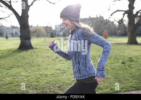 Donna sorridente runner acceso nel soleggiato parco Foto Stock