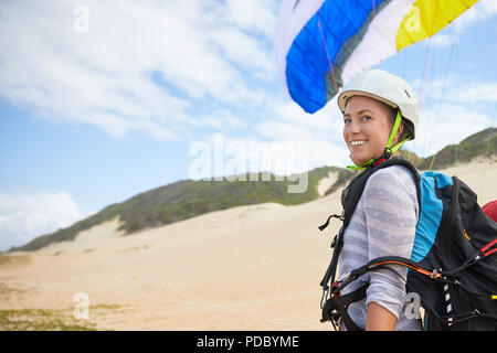 Ritratto sorridente, fiducioso giovane femmina parapendio sulla spiaggia Foto Stock