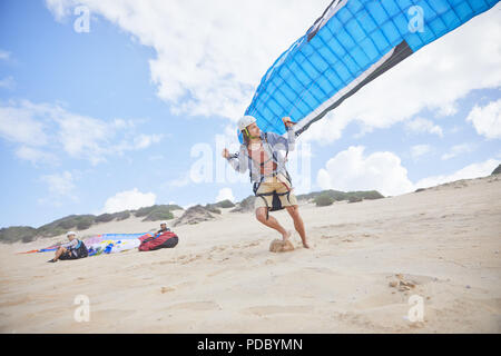 Maschio in esecuzione di parapendio con paracadute sulla spiaggia Foto Stock