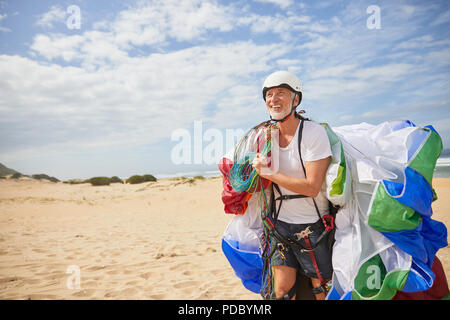 Maschio sorridente parapendio il trasporto di attrezzature e paracadute di sunny beach Foto Stock