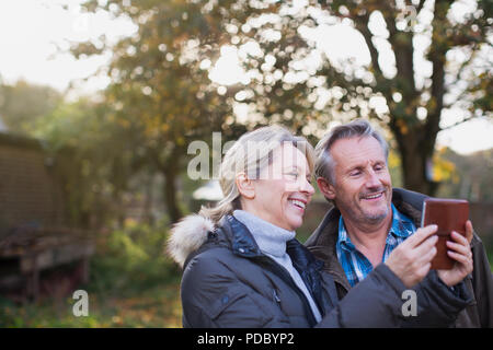 Coppia matura utilizzando smart phone in autunno backyard Foto Stock