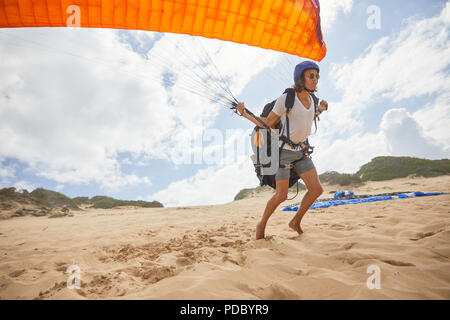 Maschio in esecuzione di parapendio con paracadute sulla spiaggia Foto Stock