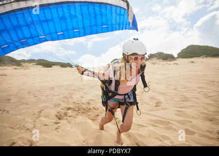 Donna sorridente parapendio in esecuzione con paracadute sulla spiaggia Foto Stock