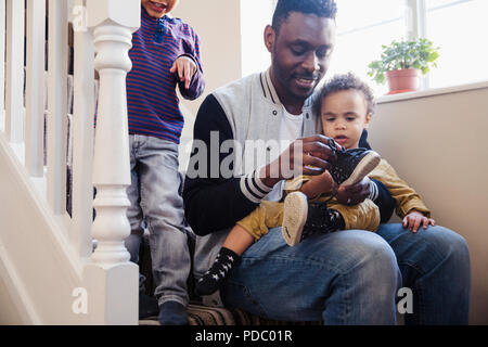 Padre mettendo le scarpe sul figlio bambino Foto Stock