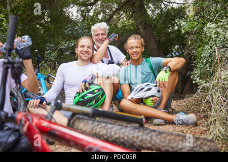 Ritratto sorridente amici maschi mountain bike, appoggiato in boschi Foto Stock