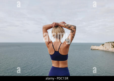 Vista posteriore di tatuati athletic ragazza in abbigliamento sportivo ed elegante in posa vicino al mare, Etretat, Francia Foto Stock