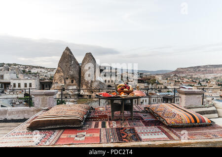 Tavola rotonda, cuscini e tappeto tradizionale sulla terrazza e belle scenic degli edifici e le rocce in Cappadocia, Turchia Foto Stock