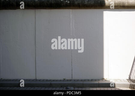 La calce e sovraverniciato sezione e segmento del muro di Berlino in parte in ombra e alla luce. Foto Stock