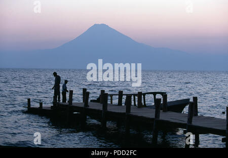 Gli uomini la pesca al largo pontile a lago Atitlan al sorgere del sole con vista del vulcano San Pedro in Guatemala pescatori sul lago Atitlan, Guatemala Foto Stock