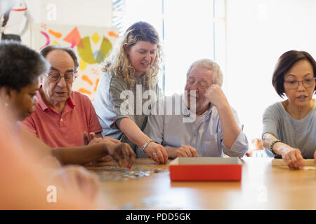 Volontariato senior aiuta l uomo assemblaggio di puzzle a tavola nel centro comunitario Foto Stock