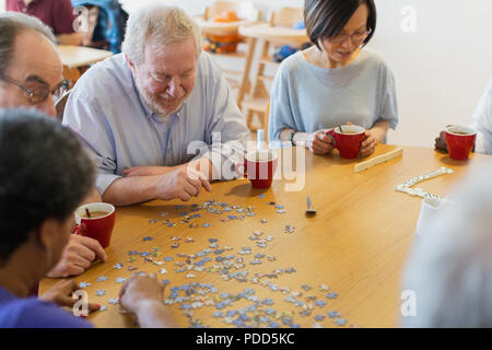 Senior amici assemblaggio di puzzle e bere il tè al tavolo nel centro della comunità Foto Stock