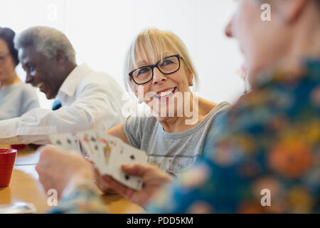 Sorridente donna senior giocando a carte con un amico in centro nella comunità Foto Stock