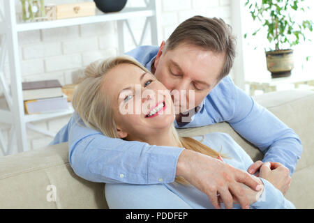 Primo piano della allegro eccitato felice felicemente felice con toothy sorriso splendente bionda attraente donna e uomo, egli abbraccia il suo da dietro e baci Foto Stock