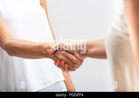 Due donne in bianco stringono le mani in un vicino la vista ritagliata concettuale del lavoro di squadra, il successo, benvenuto o accordo Foto Stock